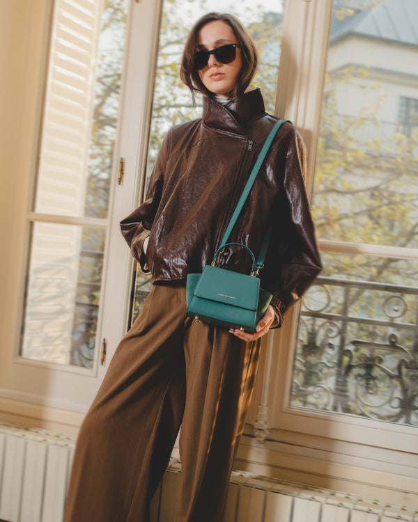ALEXIA NANO Turquoise bag, worn crossbody and held by hand, near a window