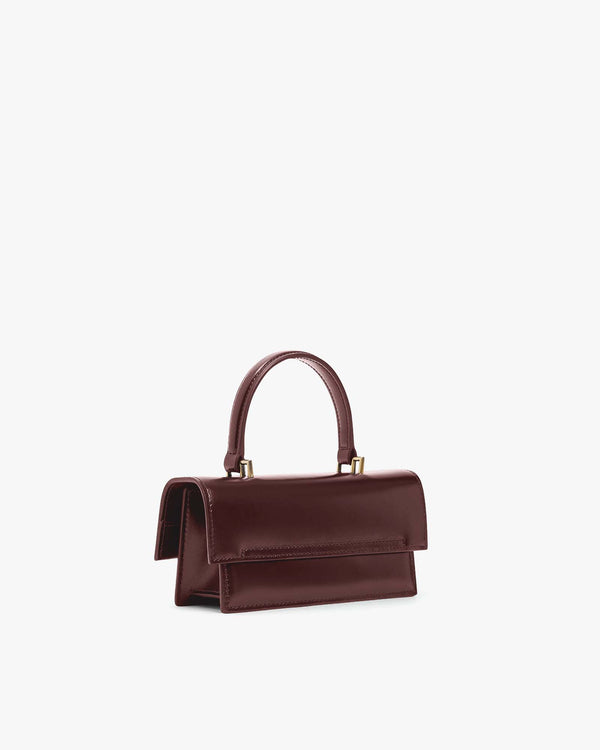 THEA MINI bag in Mahogany, side view, placed down, flap closed with top handle raised