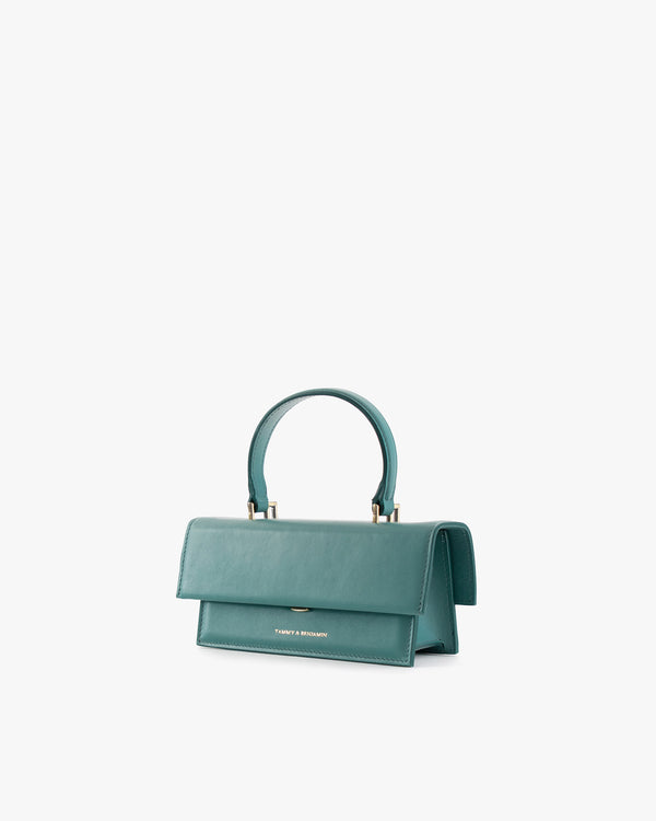 THEA MINI bag in turquoise, three-quarter view, flap closed, top handle, white background