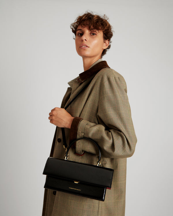 THEA bag in black naplak worn on the shoulder with top handle, side view on a model