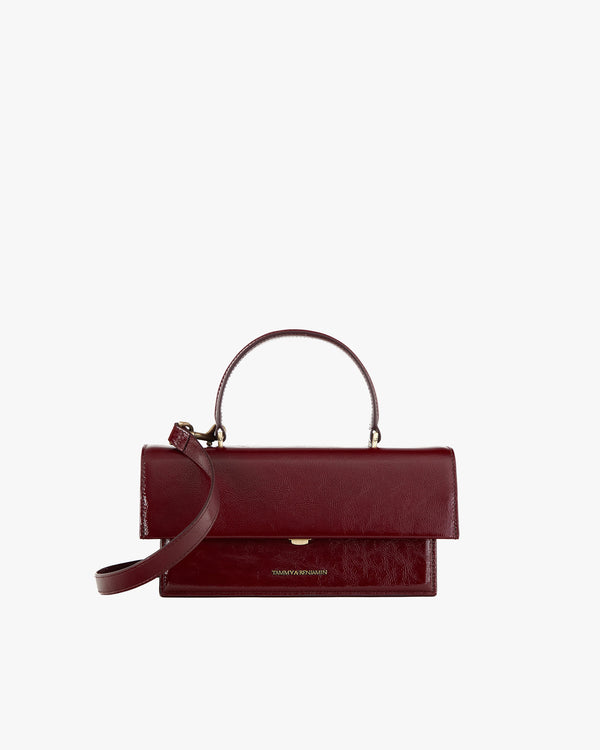 THEA bag in burgundy naplak leather, front view, standing, with oversized flap and rigid handle