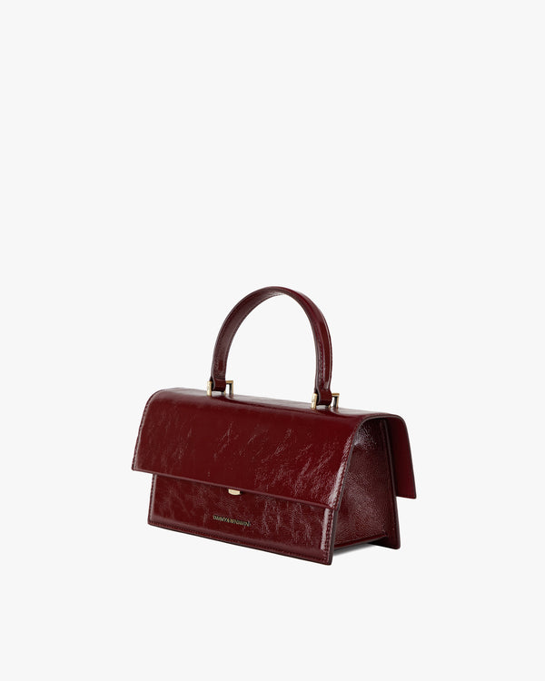 THEA bag in Bordeaux naplak, three-quarter view, oversized flap closed, standing on white background