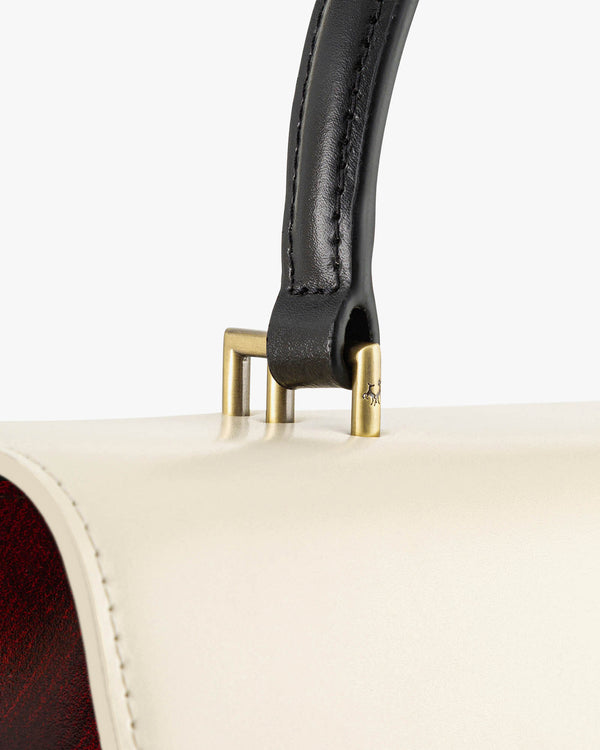 THEA bag in Colourblock art déco, close-up on brass fittings connecting the black leather handle to the cream body