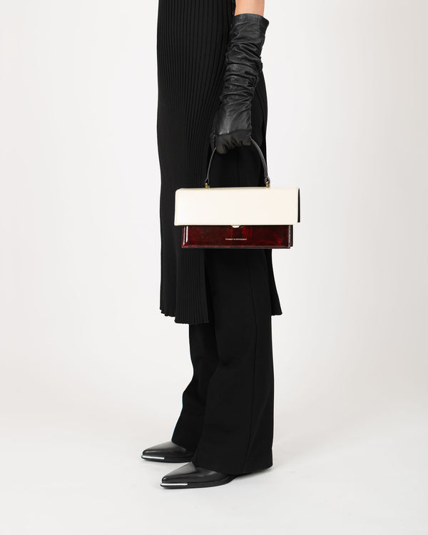 THEA Colourblock art déco bag held by its top handle, side view, off-white and burgundy colourblock