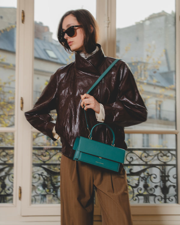 THEA turquoise bag worn crossbody, top handle, front view on a model
