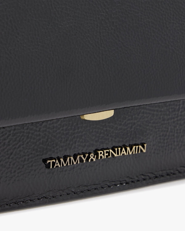 THEA MINI bag in black naplak, close-up of the gold clasp and engraved logo on the flap