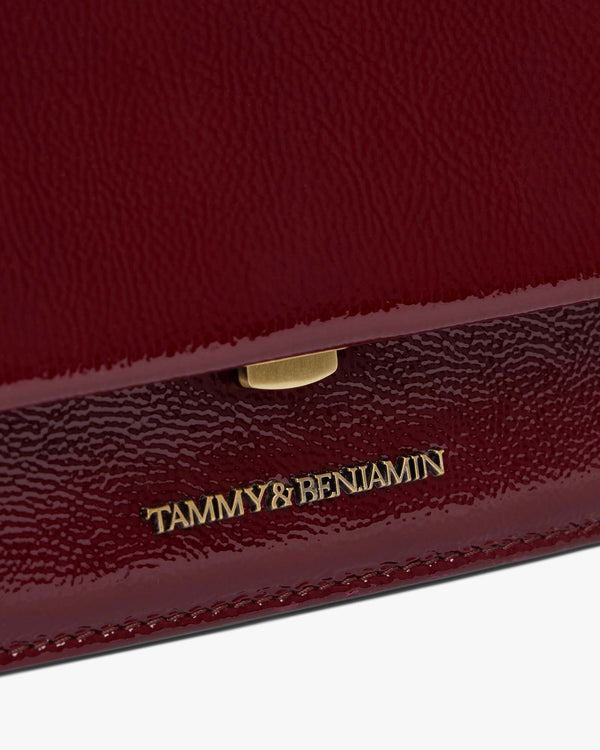 THEA MINI bag in Bordeaux naplak, close-up on the gold clasp and embossed logo on the flap