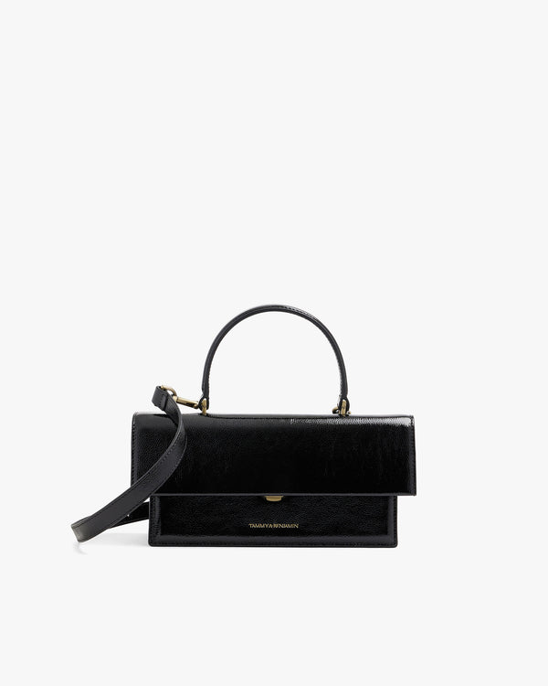 THEA bag in black naplak, front view, flap closed, rigid handle and adjustable strap attached
