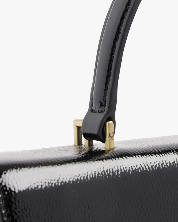 THEA in black naplak, close-up of the handle attachment with gold hardware and embossed logo