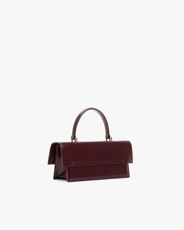 THEA bag in Mahogany, rear three-quarter view, standing, flap closed, top handle raised