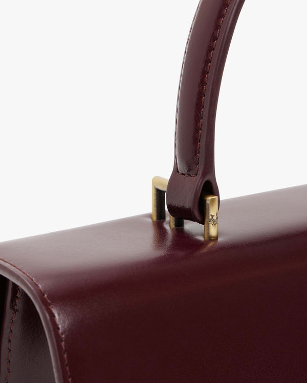 THEA bag in Mahogany, close-up of the rigid handle and gold-tone hardware